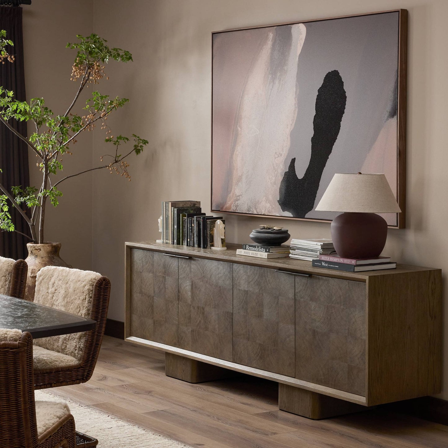 A modern living room features the Salta Sideboard (95.25"w x 20.00"d x 32.25"h) with books, a lamp, and decor, abstract art above, plus a dining table with textured chairs and a leafy plant on the wooden floor.