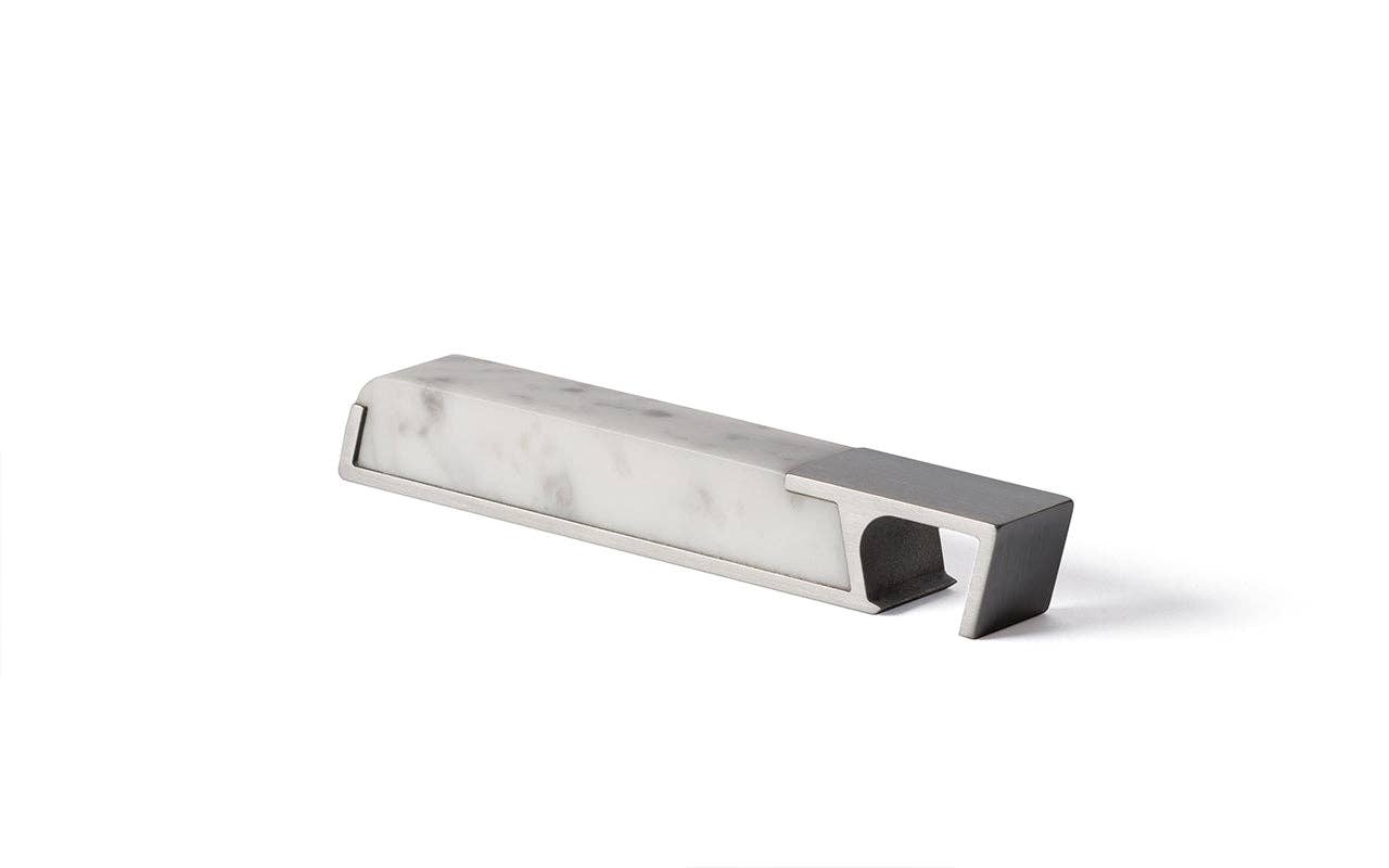 A modern, minimalist bottle opener with a rectangular shape, featuring heirloom-quality brushed metal and a white marble-like center, set against a plain white background. Product: Modern Marble Bottle Opener.