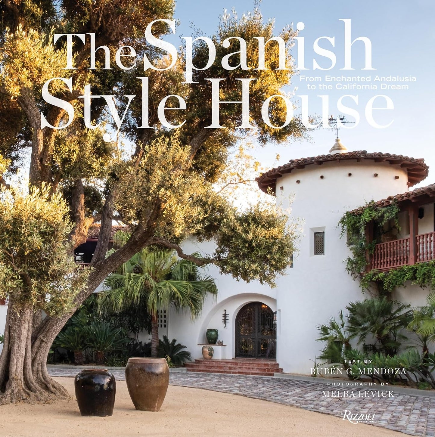 Front cover of The Spanish Style House, showcasing a classic Spanish-style home with white stucco walls, terracotta roof tiles, an arched door, a large tree, potted plants, and abundant greenery. This beautifully photographed 9″x9″ book by Ruben G. Mendoza and Melba Levick highlights the timeless elegance and charm of Spanish-style architecture.