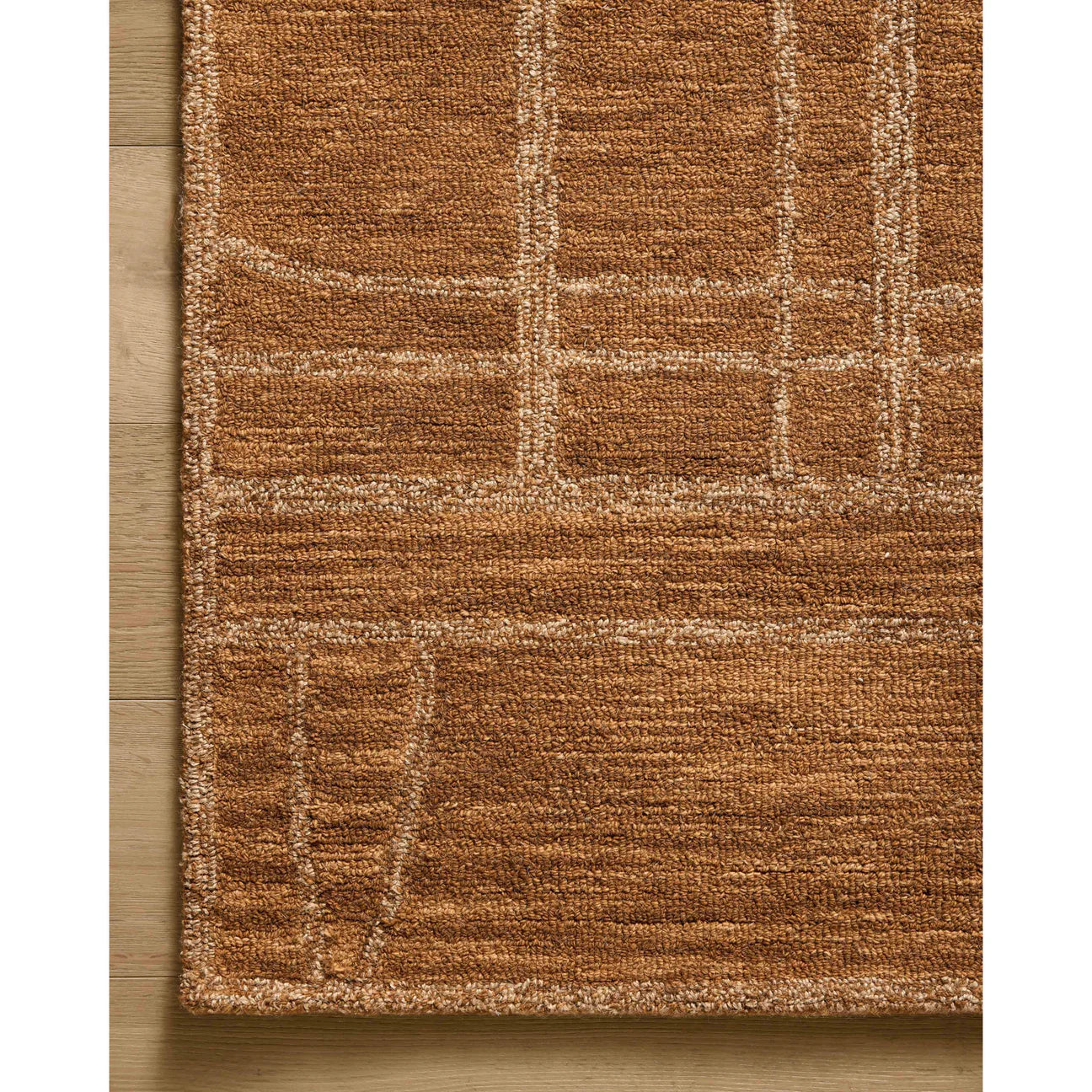 A close-up of the Burnt Orange Patterned Rug showcases its rich textured surface with a subtle geometric pattern in lighter beige tones, displayed on a light wooden floor. Measuring 5'x7'6", this rug is an ideal choice for various living spaces.