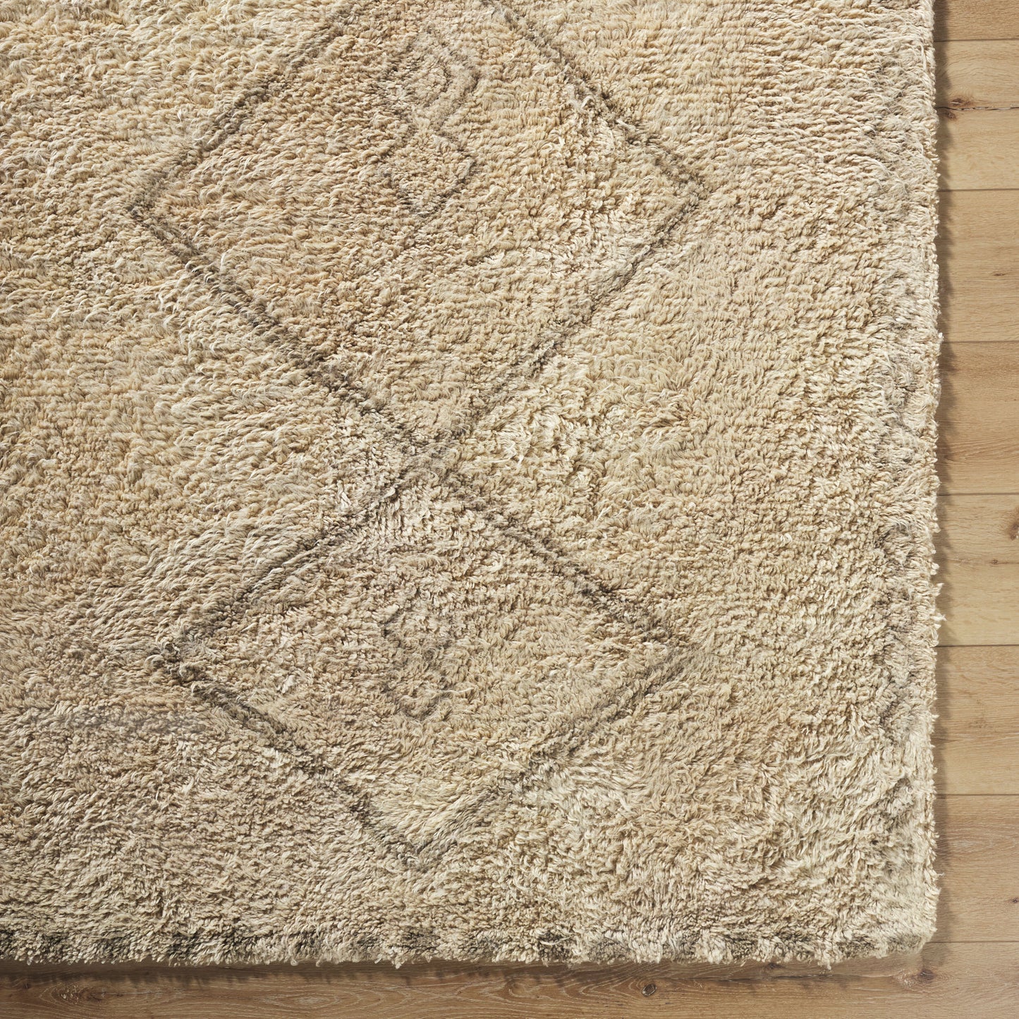 An 8'x10' Beige Moroccan Wool Rug with faint diamond patterns and thick shaggy texture rests on a wooden floor, its subtle geometric design partially visible.