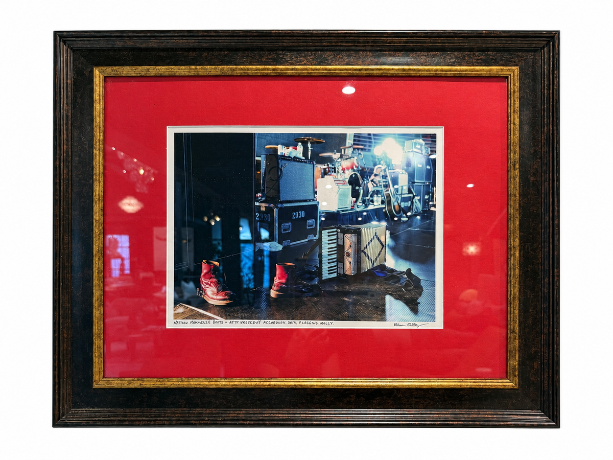 Framed 24.5x20.5 Flogging Molly Stage Print of a concert stage with red boots and an accordion resting on the floor in front of musical equipment.