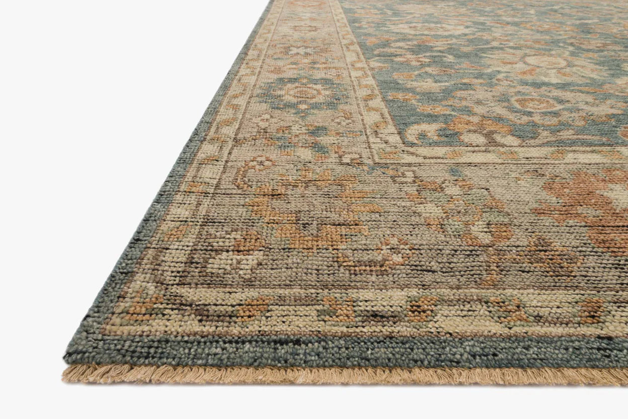 A close-up of the Blue Beige Traditional Pattern Rug shows its intricate floral design, decorative border, and short tan fringe. Crafted from wool and cotton in muted blue, beige, and rust tones, it’s available in various sizes.