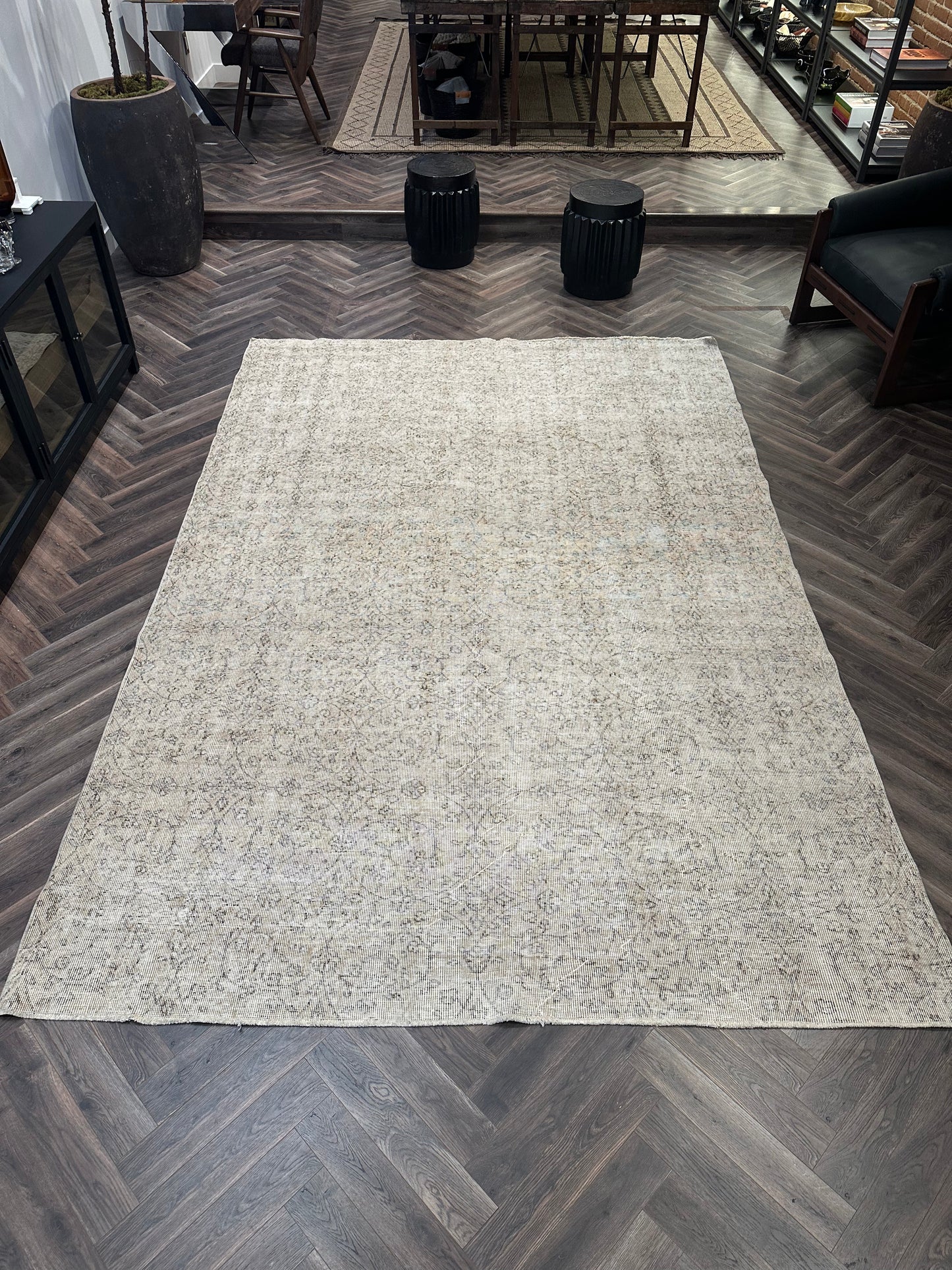 A Reversible Vintage Rug with a subtle pattern is laid out on a dark herringbone wood floor in a modern room featuring black furniture and decor.