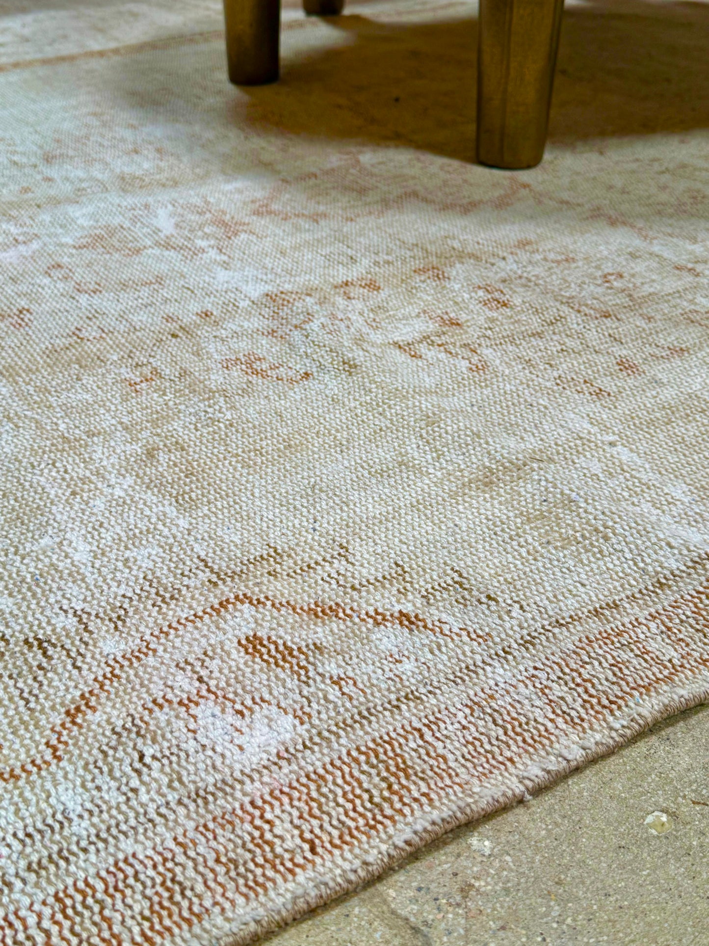 A close-up of the Vintage Cream/Sienna Reversible Rug, featuring textured beige and light brown tones and measuring 8'10" x 4'8", displayed on a tiled floor with the legs of a wooden table visible in the background.