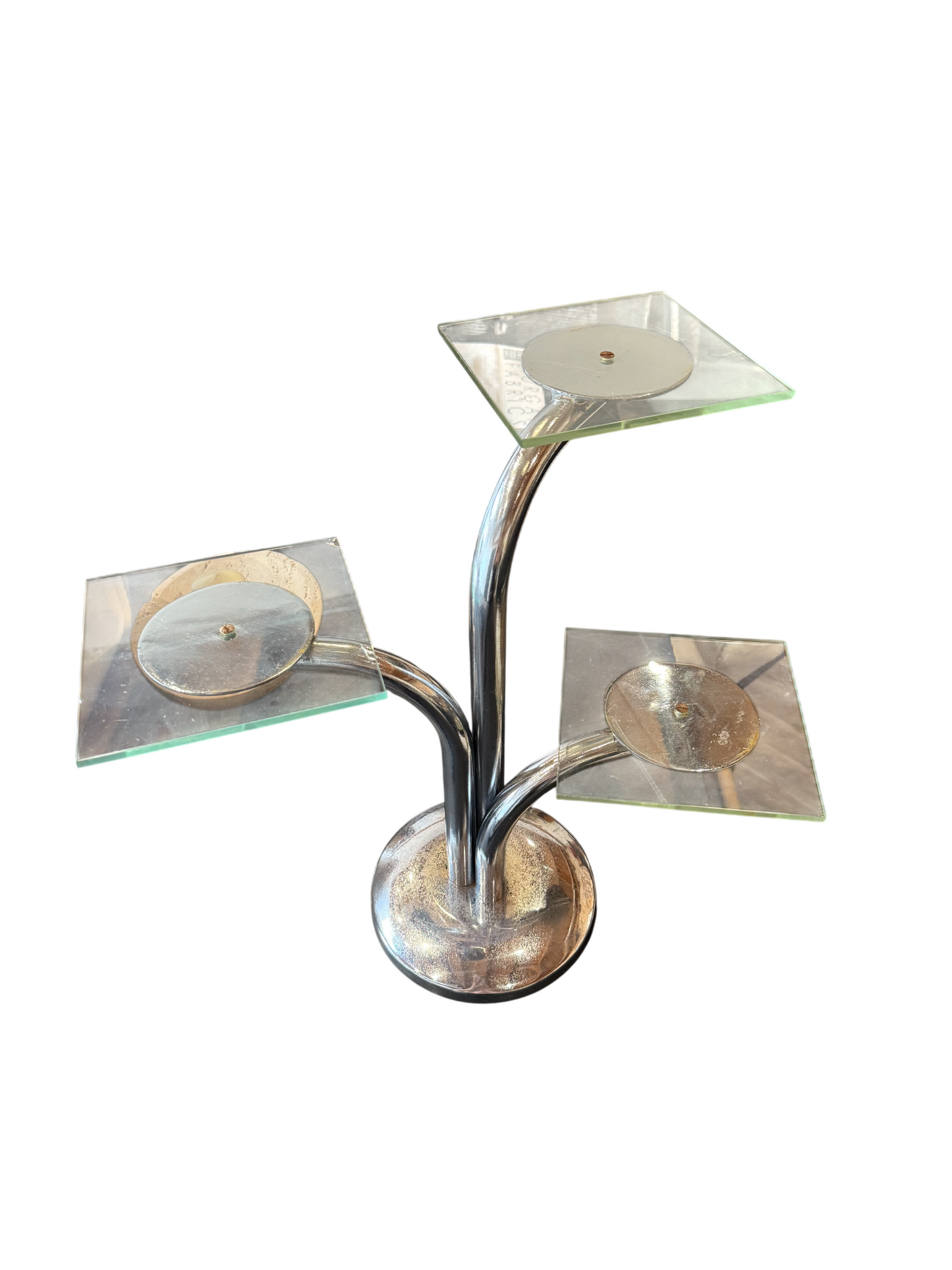 The Chrome Candle Holder is a metal stand featuring three curved arms, each supporting a square glass platform, perfect for displaying items or holding candles. Its overall dimensions are 20″w x 12″d x 17″h.