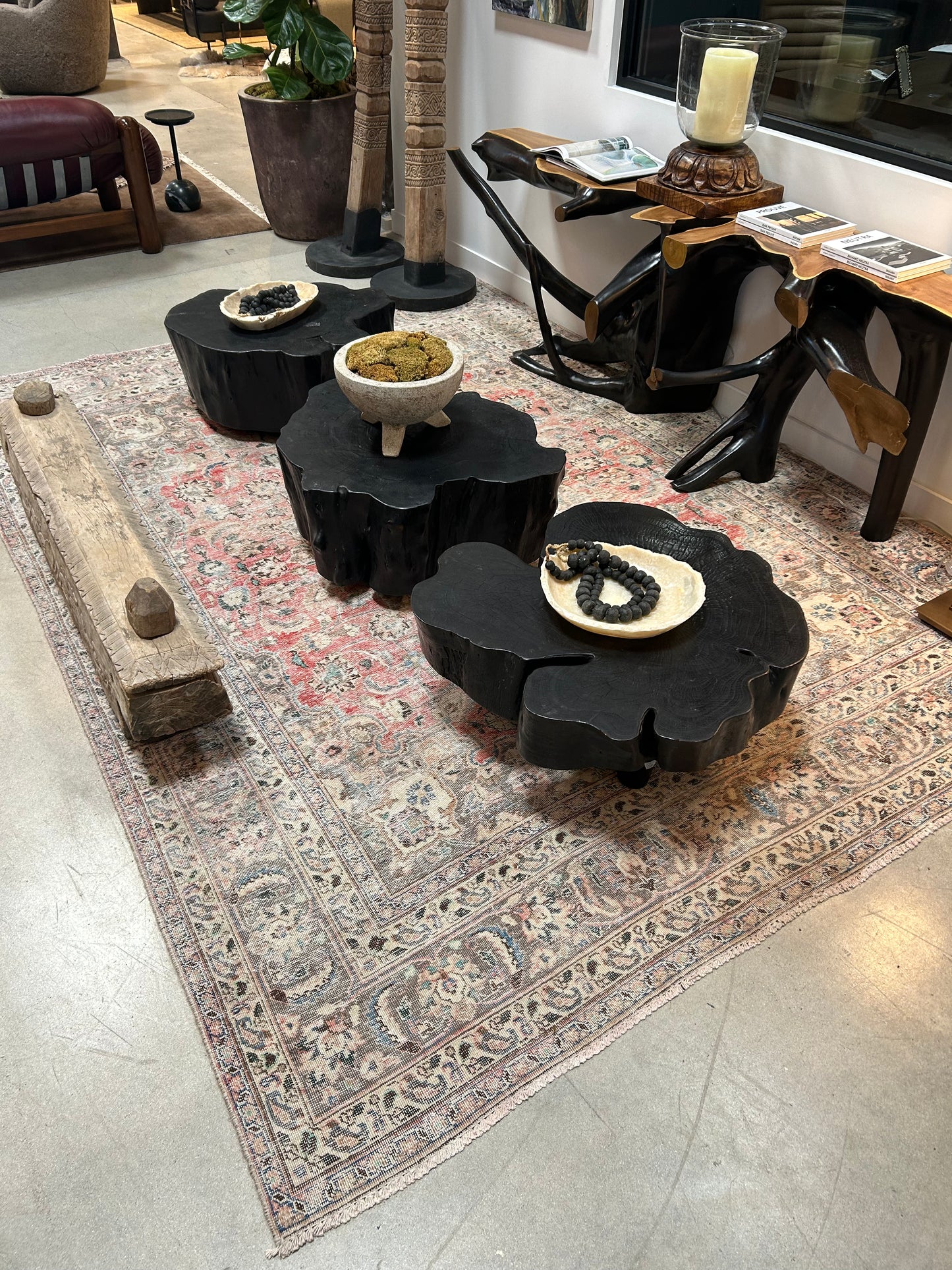 A Vintage Area Rug in ivory, grey, and pink anchors the cozy modern room (11'3" x 8'), with three black organic coffee tables topped with decorative bowls and beads. Unique wood furniture and a wooden beam complete the look.