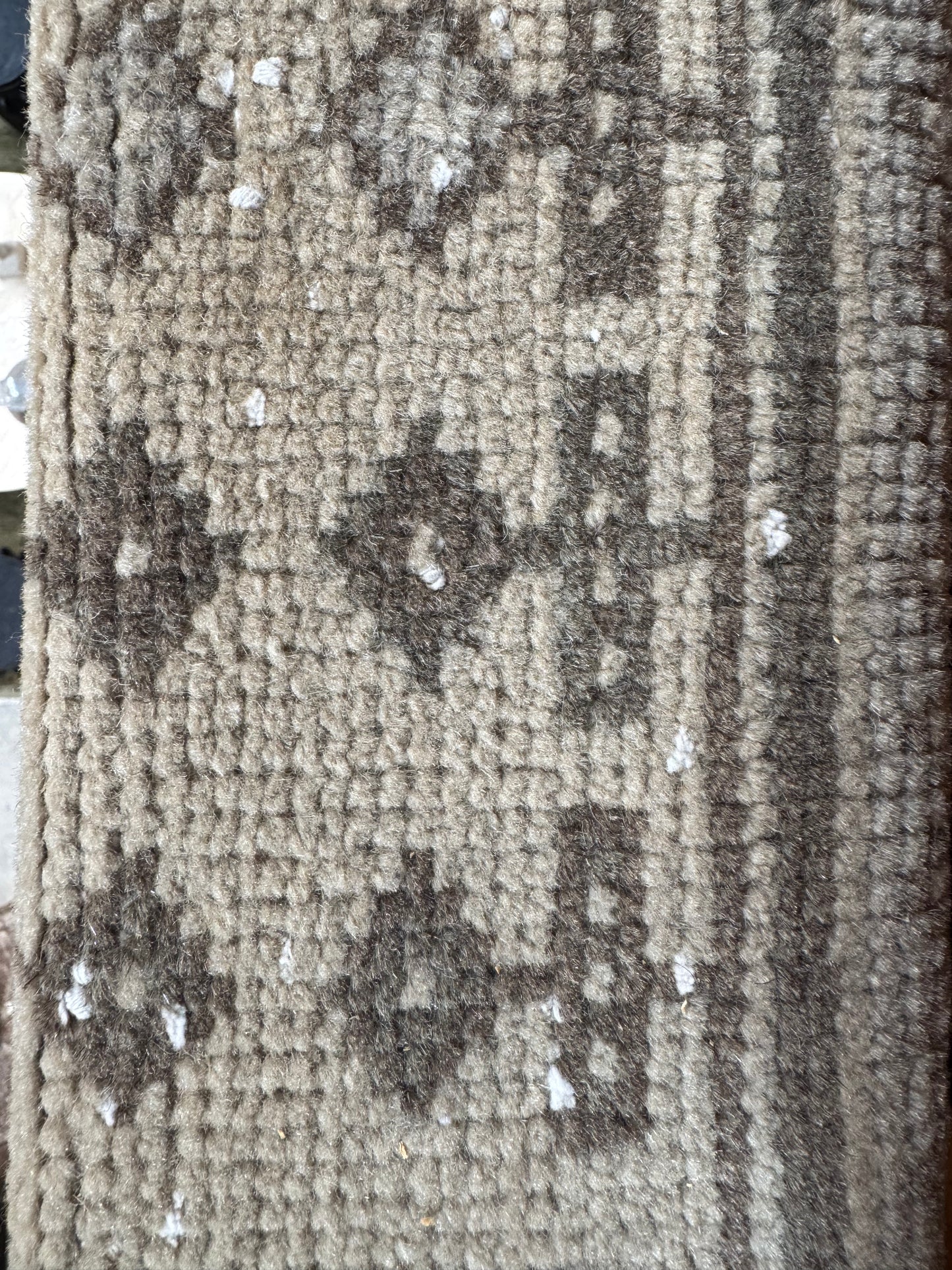 A close-up of the Vintage Turkish Runner Rug in beige and brown geometric patterns, with small white debris scattered across its surface.