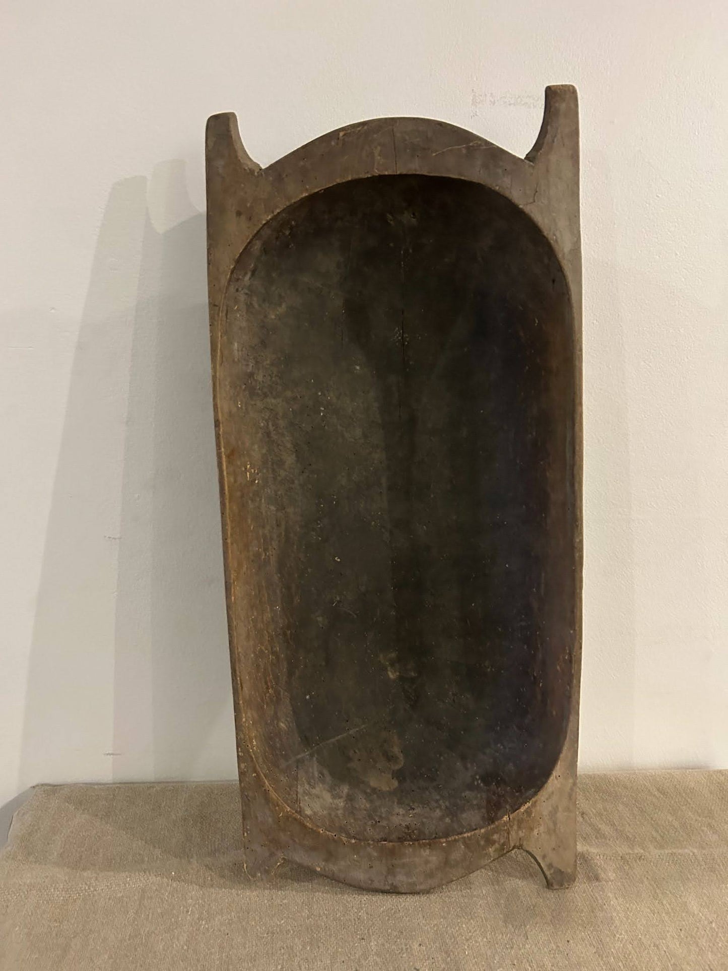 The Large Dark Display Bowl is a big, oval wooden bowl with tall sides and end handles—shown upright on a fabric surface—ideal for repurposing as a rustic 33-inch dog bed or unique large pet bed.