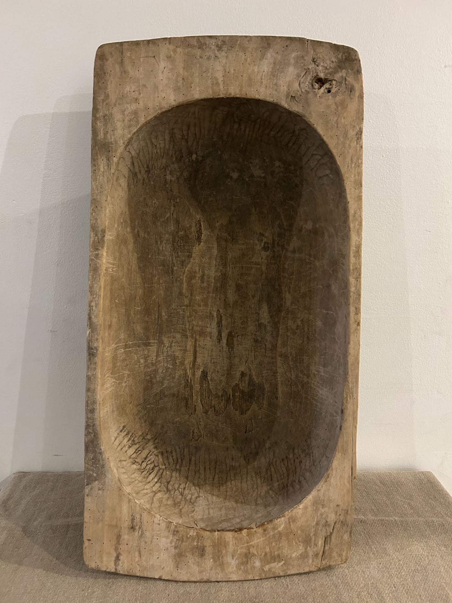 The Large Light Display Bowl, a rectangular rustic wooden piece with a deep carved interior, stands upright against a light wall on a textured surface, evoking the organic charm of vintage bathtub dimensions and classic tub styles.