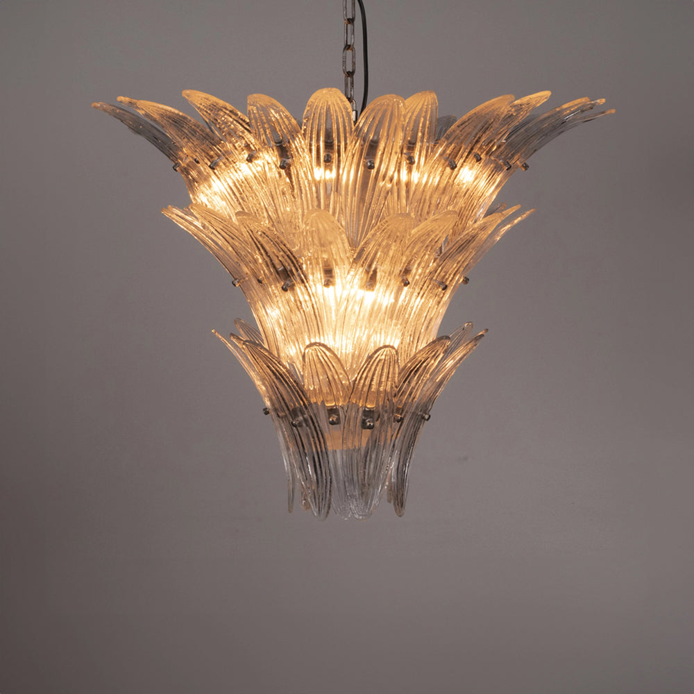 The Murano-inspired Chandelier features layered, petal-like clear glass pieces that radiate outward, casting a warm glow against a light-gray background.