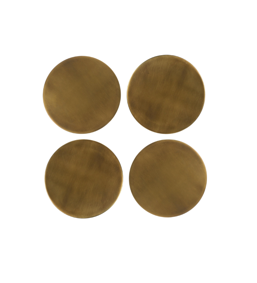 The Brass Coasters (Set of 4) features round, flat brass coasters with a matte finish and a 4-inch diameter, shown arranged in a 2x2 grid on a white background.