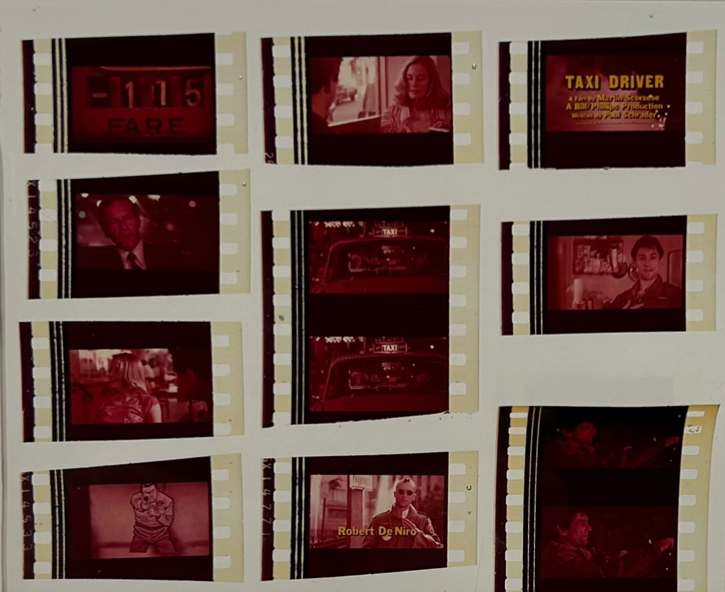 The Movie Reel in Acrylic showcases film negatives from Taxi Driver, featuring character close-ups, a taxi meter, and the movie title. With a reddish tint and visible sprocket holes, this collectible is perfect for fans.