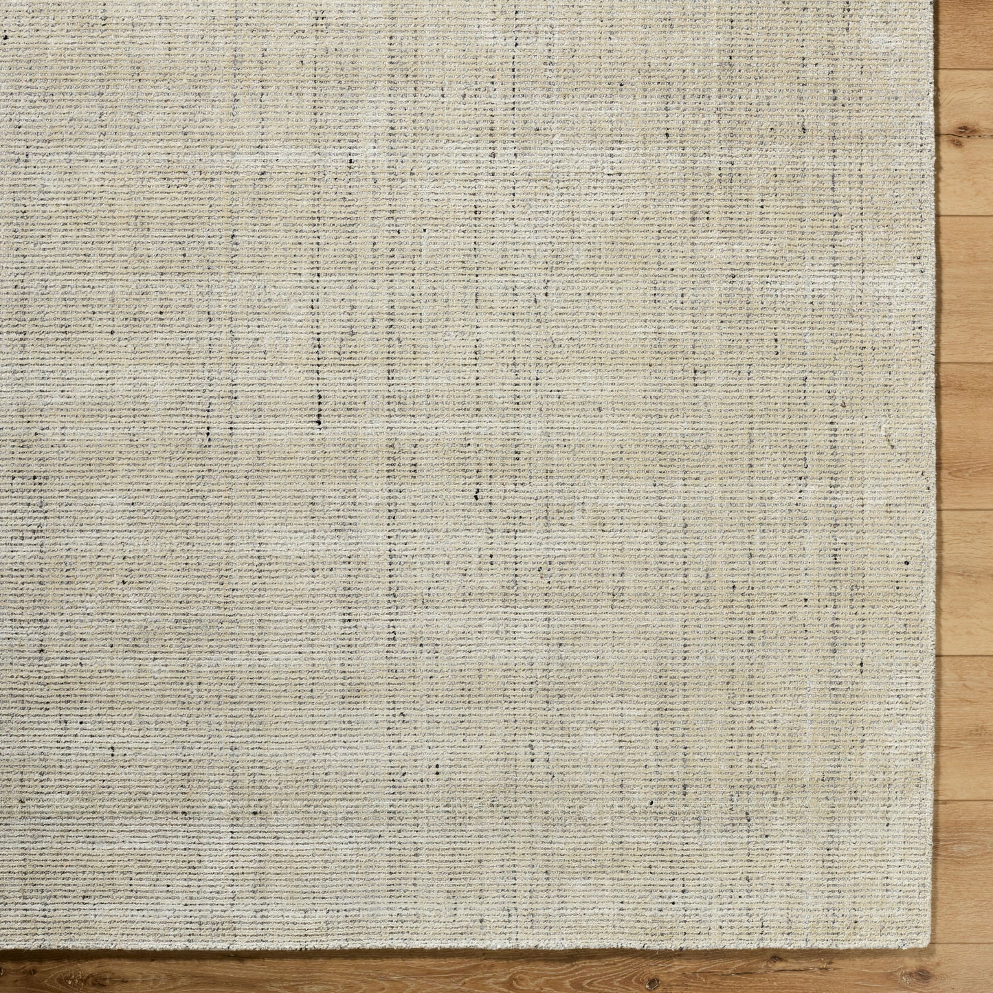 A close-up of the Viscose and Wool Rug - 8'x10' in beige on a wood floor highlights its textured surface and subtle pattern, with natural wood visible along the right and bottom edges.