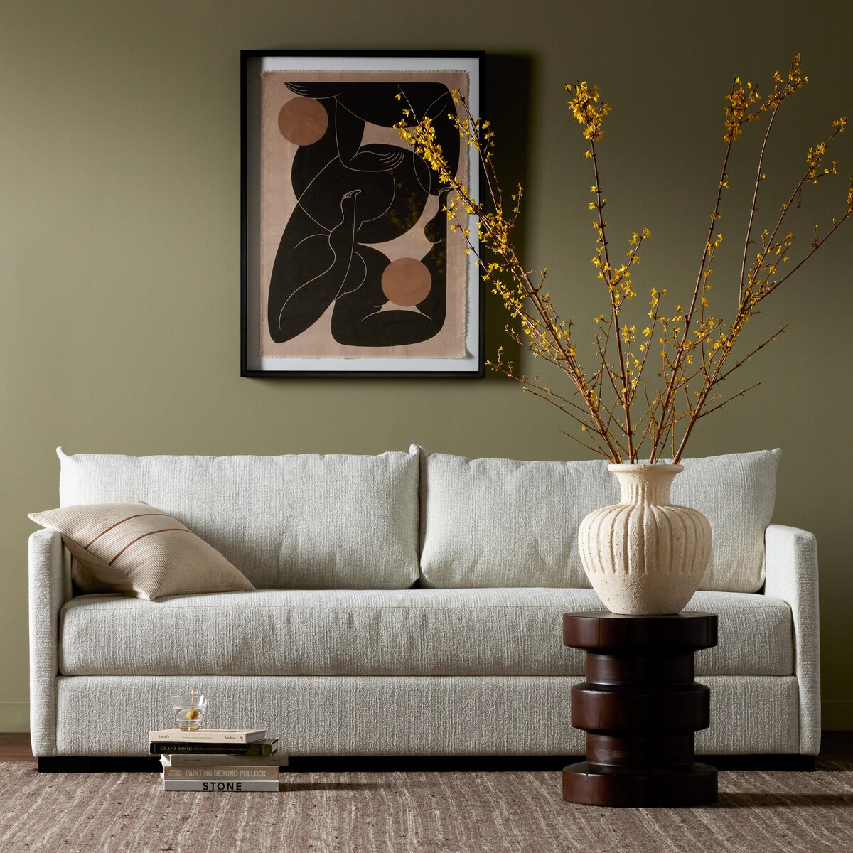 A modern living room featuring the Classic Sofa Bed in light gray, beige pillow, abstract wall art, stacked wooden side table, large cream vase with yellow branches, and brown textured rug—great inspiration for Queen or twin bed upholstery choices.