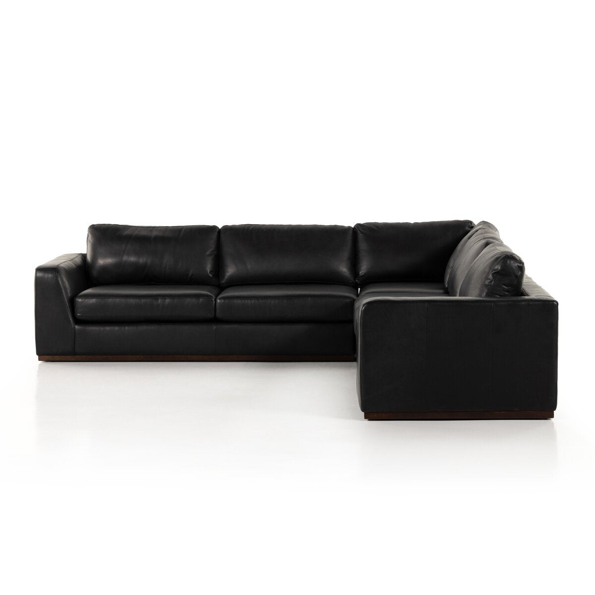 The Simple Modular Corner Sectional is a modern black leather sofa with clean lines, plush seat and back cushions, low wooden legs, and heirloom Italian leather, shown against a white background.