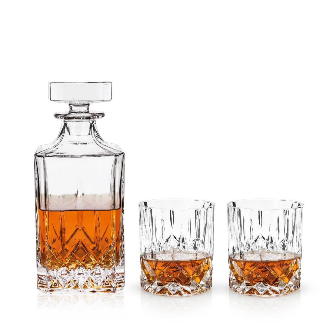 The Crystal Whiskey Decanter and Tumblers (Set of 3) features a lead-free crystal decanter filled with amber liquor beside two matching glasses, each poured with whiskey, elegantly arranged against a white background.