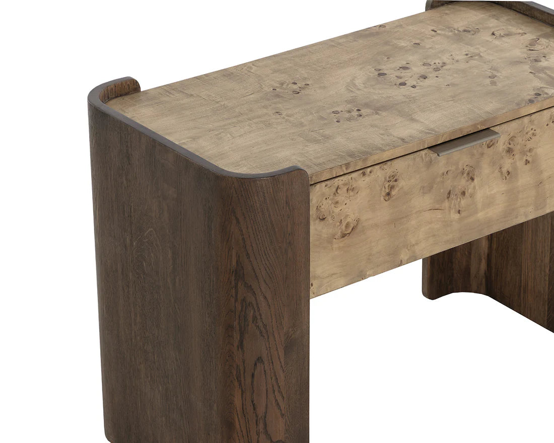 A close-up of the Two-Toned Wooden Nightstand shows its modern design. The natural wood tabletop and drawer contrast with darker mappa burl veneer sides and solid oak legs, all featuring rounded edges for a stylish look.