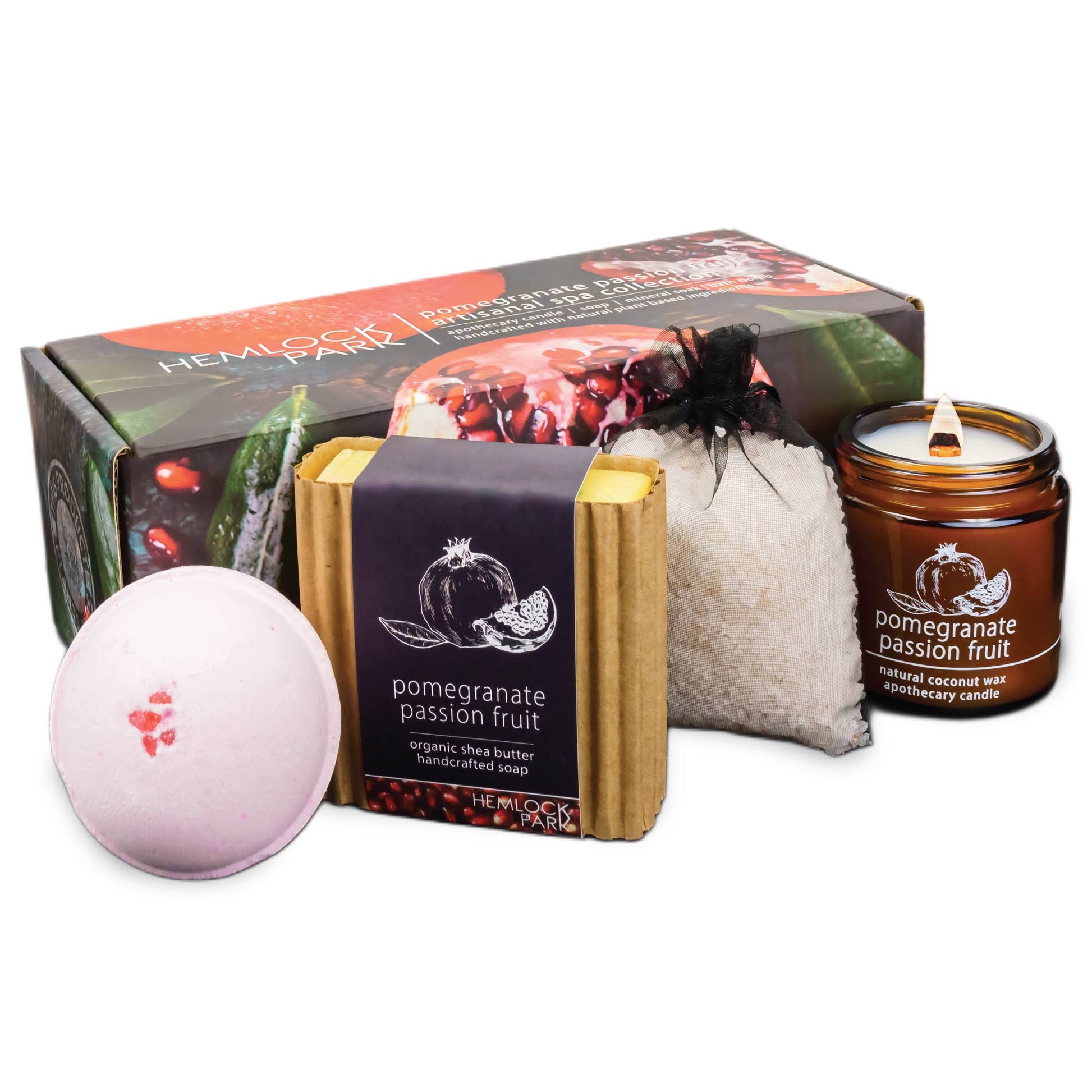 The Artisanal Spa & Candle Gift Box includes a pomegranate-inspired bath bomb, soap with organic shea butter, calming bath salts, and a petite candle—all elegantly presented before a decorative box featuring a pomegranate design.