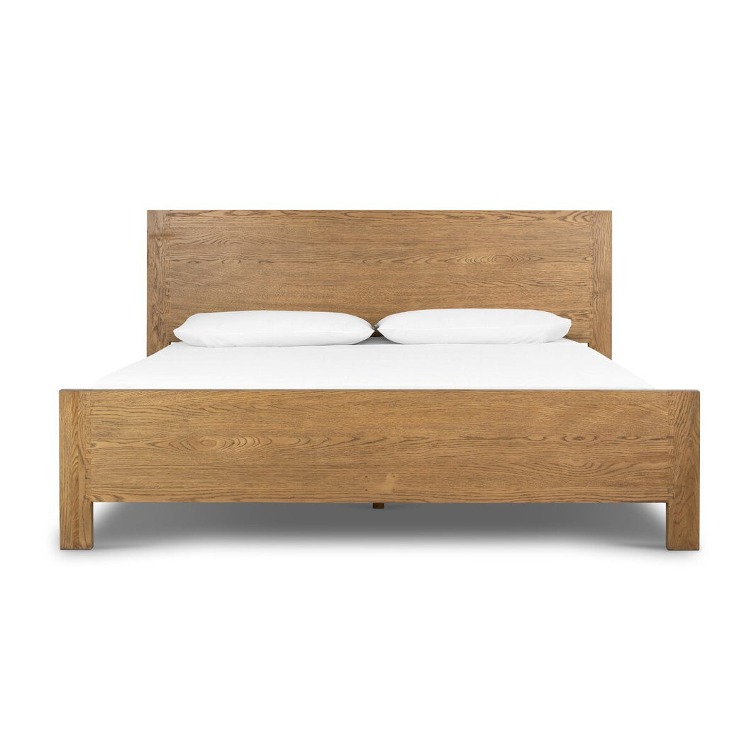 The Tawny Oak Bedframe, shown front-facing in queen size, features a simple headboard, natural wood finish, white bedding with two white pillows, and a clean minimalist design.
