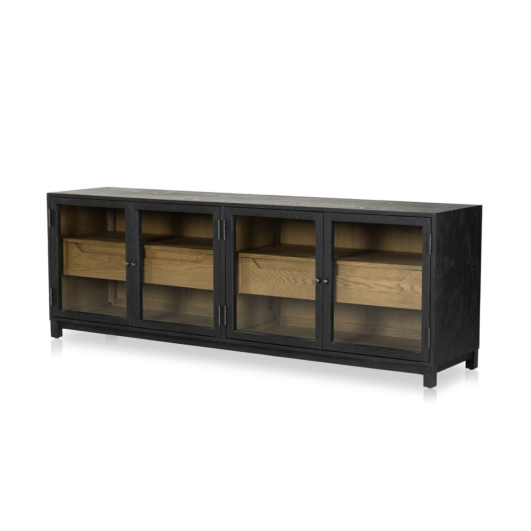 The Two-Tone Glass Media Cabinet features a modern black drifted oak finish with three glass doors that showcase natural wood shelves and interior drawers, photographed against a white background.