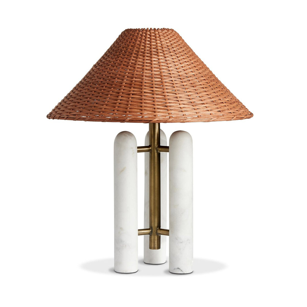 The Marble and Rattan Table Lamp features a wide woven rattan shade, a brass central stem, and three cylindrical white marble legs, displayed against a white background.