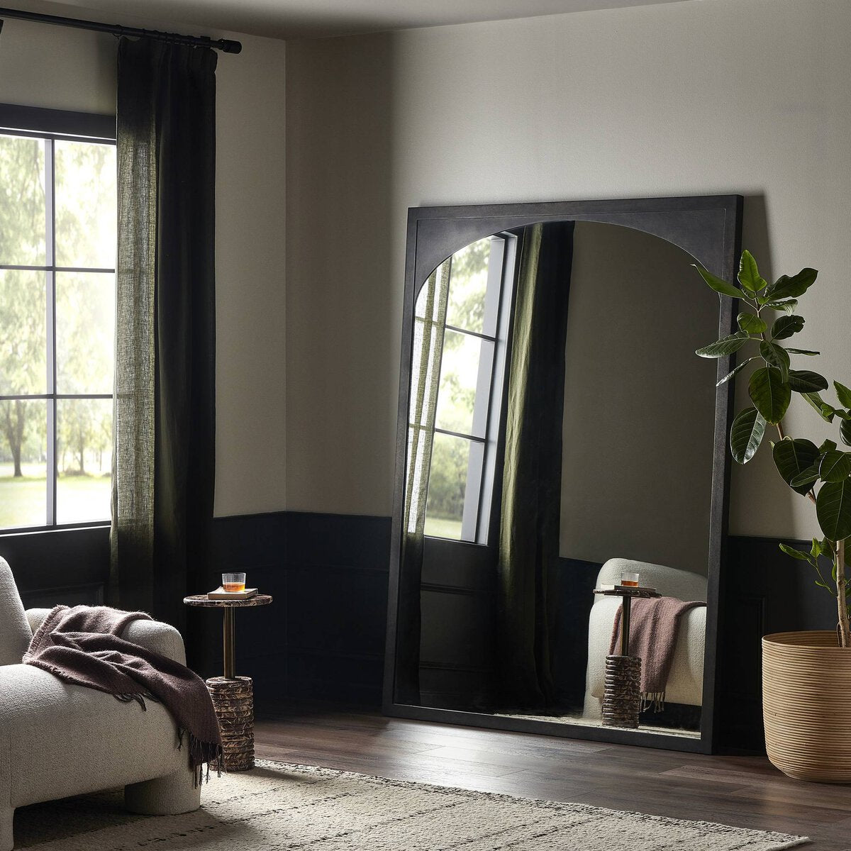 Troyes Floor Mirror, a large arched mirror with a black frame measuring 60.00″w x 2.00″d x 79.50″h, leaning against a living room wall.