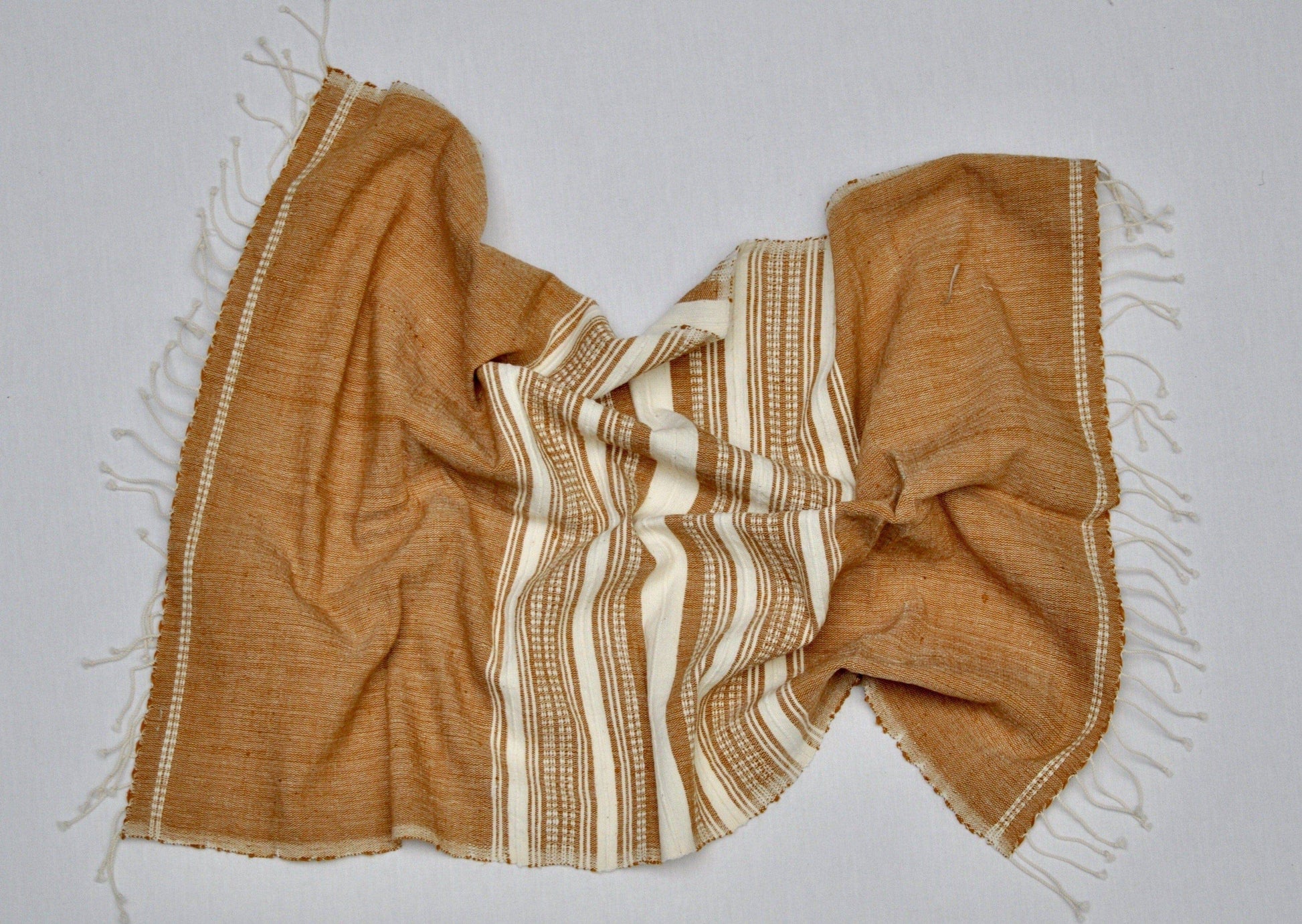 A Handwoven Ethiopian Cotton Hand Towel in brown and cream stripes with fringed edges is displayed on a flat surface, artfully gathered in the center and spread at the sides, showcasing traditional Ethiopian craftsmanship.