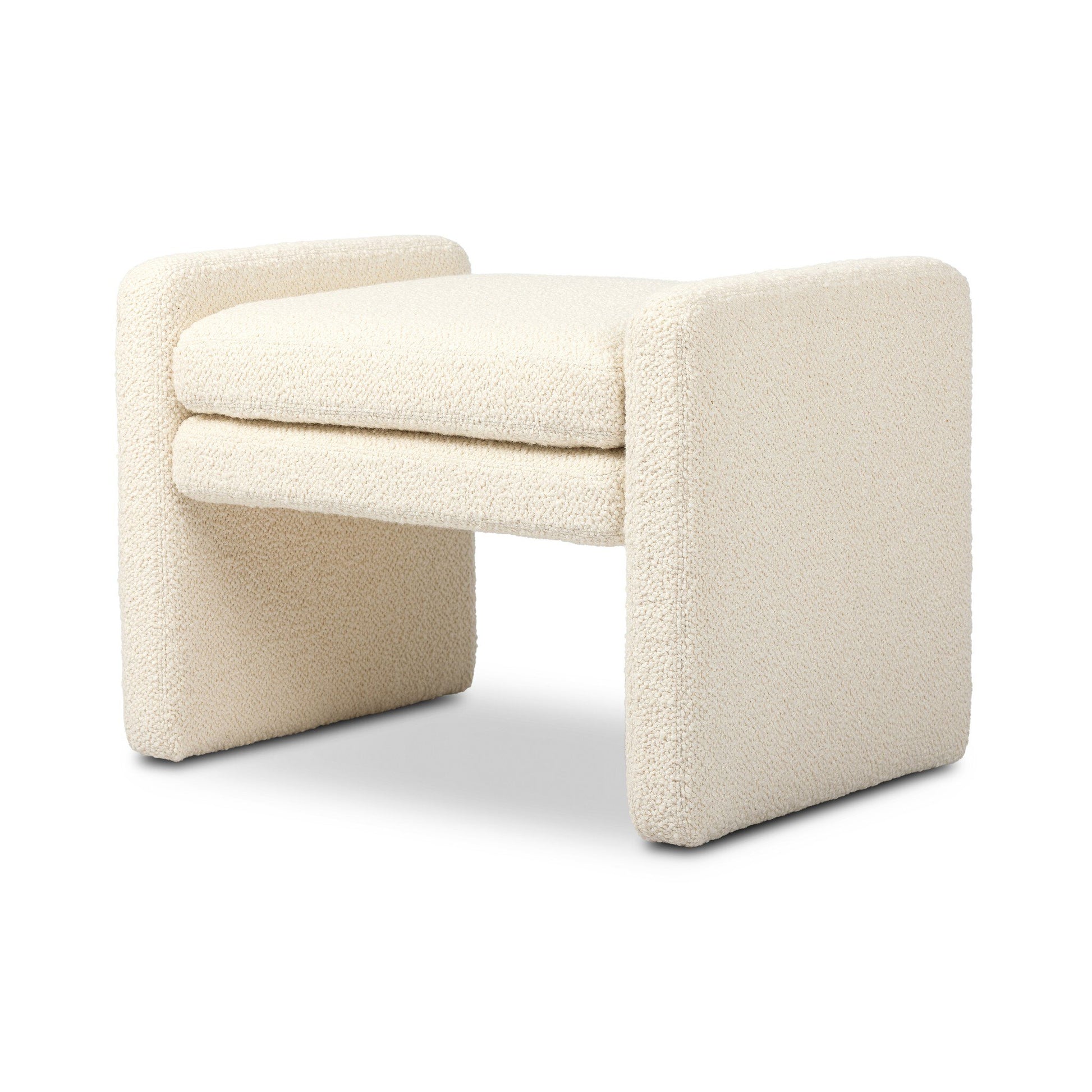 The Serena Ottoman is a modern, minimalist cream bench featuring a cushioned seat, thick rectangular supports, and soft textured fabric upholstery. Its compact 26.00"w x 18.00"d size allows versatile placement in any space.