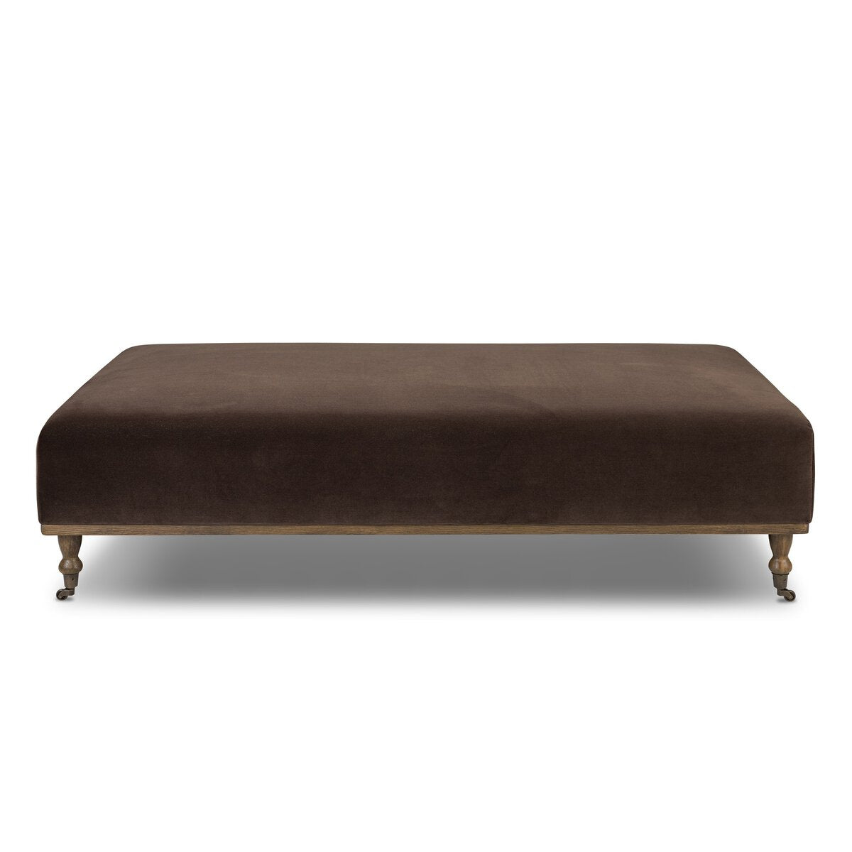 The Harlin Cocktail Ottoman is a rectangular brown upholstered piece with short turned wooden legs and casters, ideal as a modern accent or paired with a sofa table in your living room, shown against a white background.