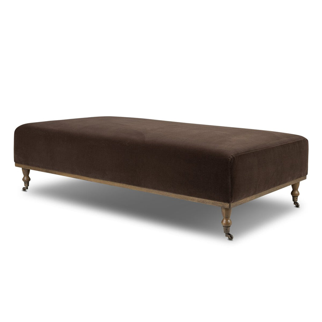 The Harlin Cocktail Ottoman is a rectangular, dark brown upholstered piece with wooden legs and small caster wheels, perfect as modern living room furniture, pictured against a white background.