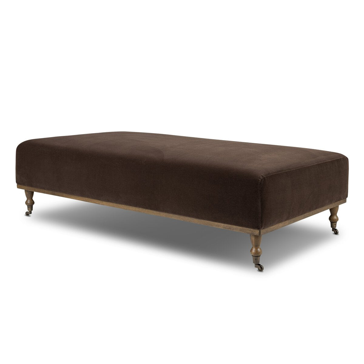 The Harlin Cocktail Ottoman is a rectangular, dark brown upholstered piece with wooden legs and small caster wheels, perfect as modern living room furniture, pictured against a white background.