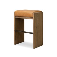 The Nash Bar + Counter Stool is shown against a white background, featuring a tan leather cushioned seat, rectangular wooden sides, and a black metal footrest bar. Please inquire for dimensions.