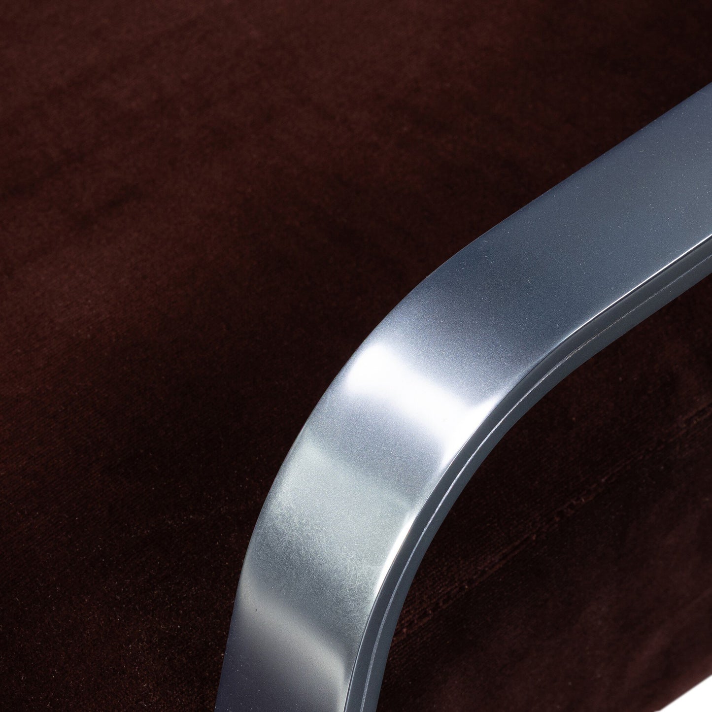 Close-up of the shiny, curved metal armrest on the plush, dark brown upholstery of the Lou Desk Chair; dimensions: 23.25"w x 28.50"d x 37.25"h.