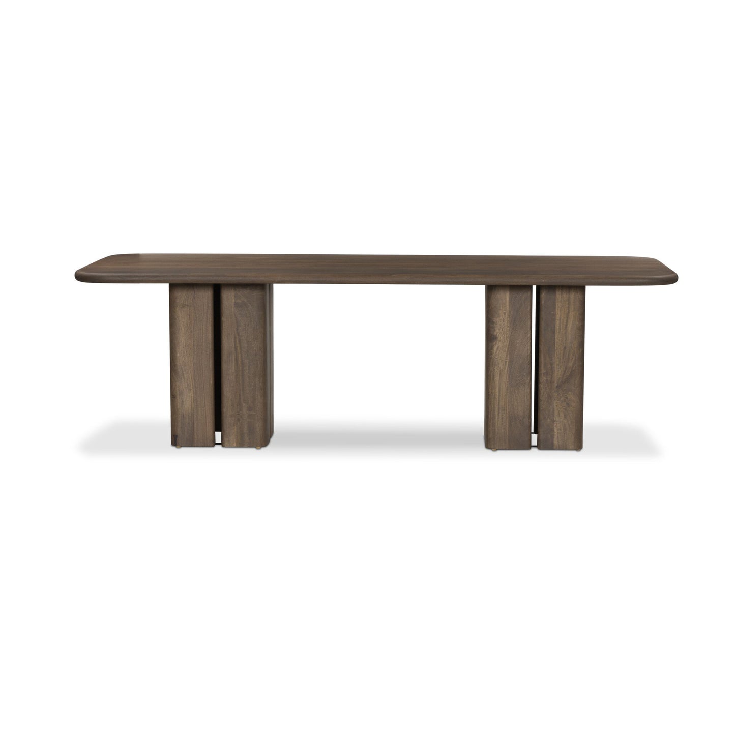 The Rishi Dining Table is a modern rectangular wooden table with rounded corners and two wide, block-style legs featuring a central vertical groove, set against a plain white background.