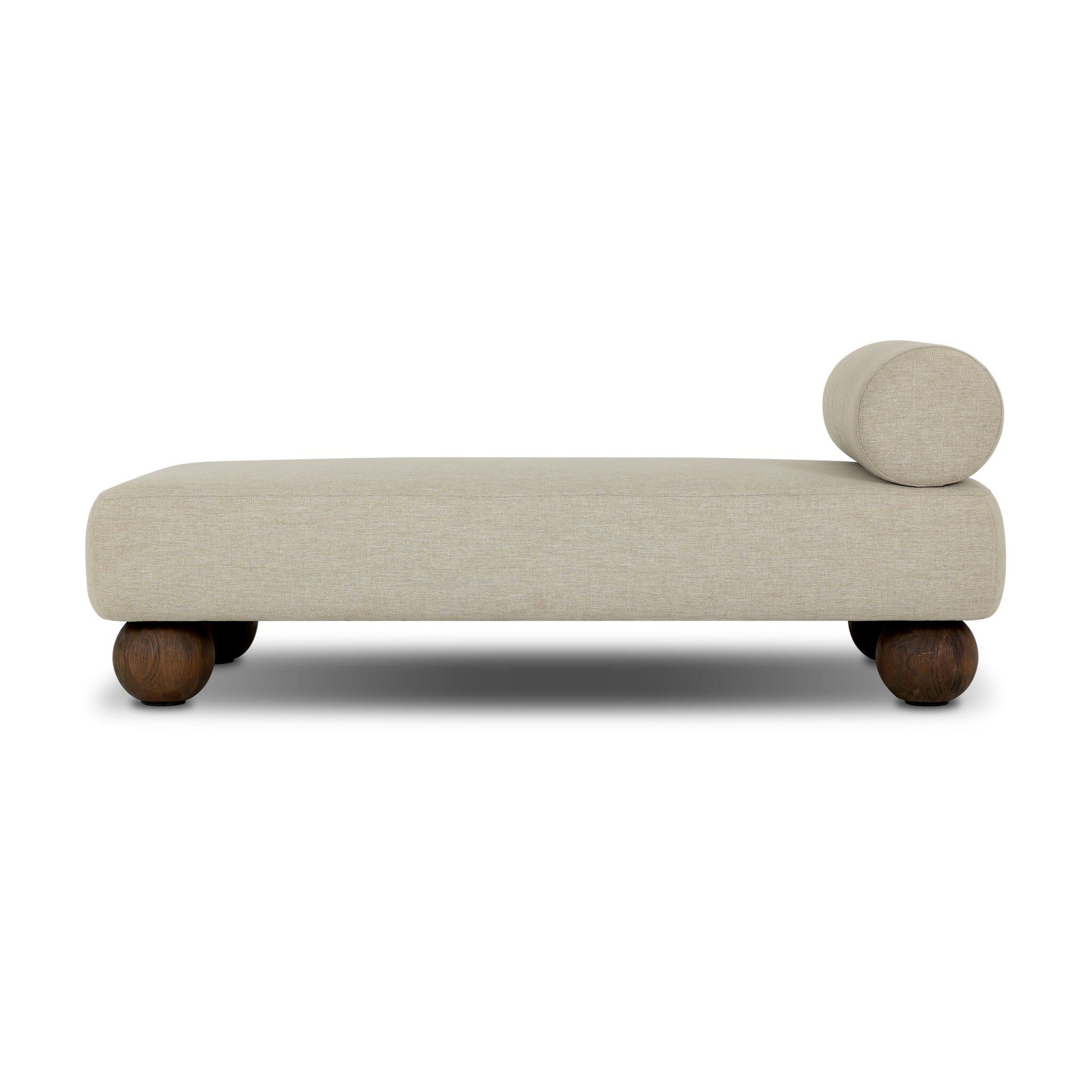 The Leilani Outdoor Chaise features modern beige upholstery, a cylindrical bolster pillow at one end, and four rounded dark wooden legs—ideal beside an office desk or in a contemporary workstation, pictured against a white background.