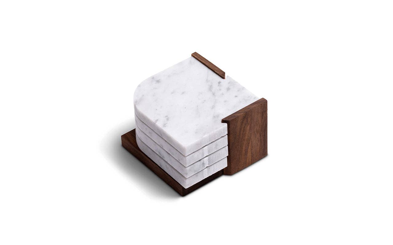 The Marble Coasters + Trivet set features four white marble coasters with rounded edges, stacked neatly in a walnut stand and shown against a white background.