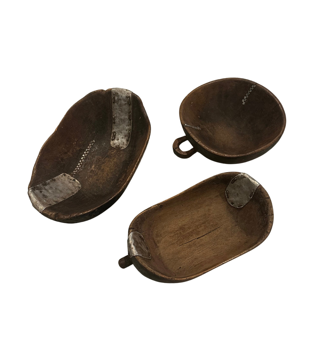 The Wood and Metal Bowls feature unique rustic wooden designs with metal patches and handles, available in assorted shapes and sizes. Each bowl is sold individually. Displayed on a white background.