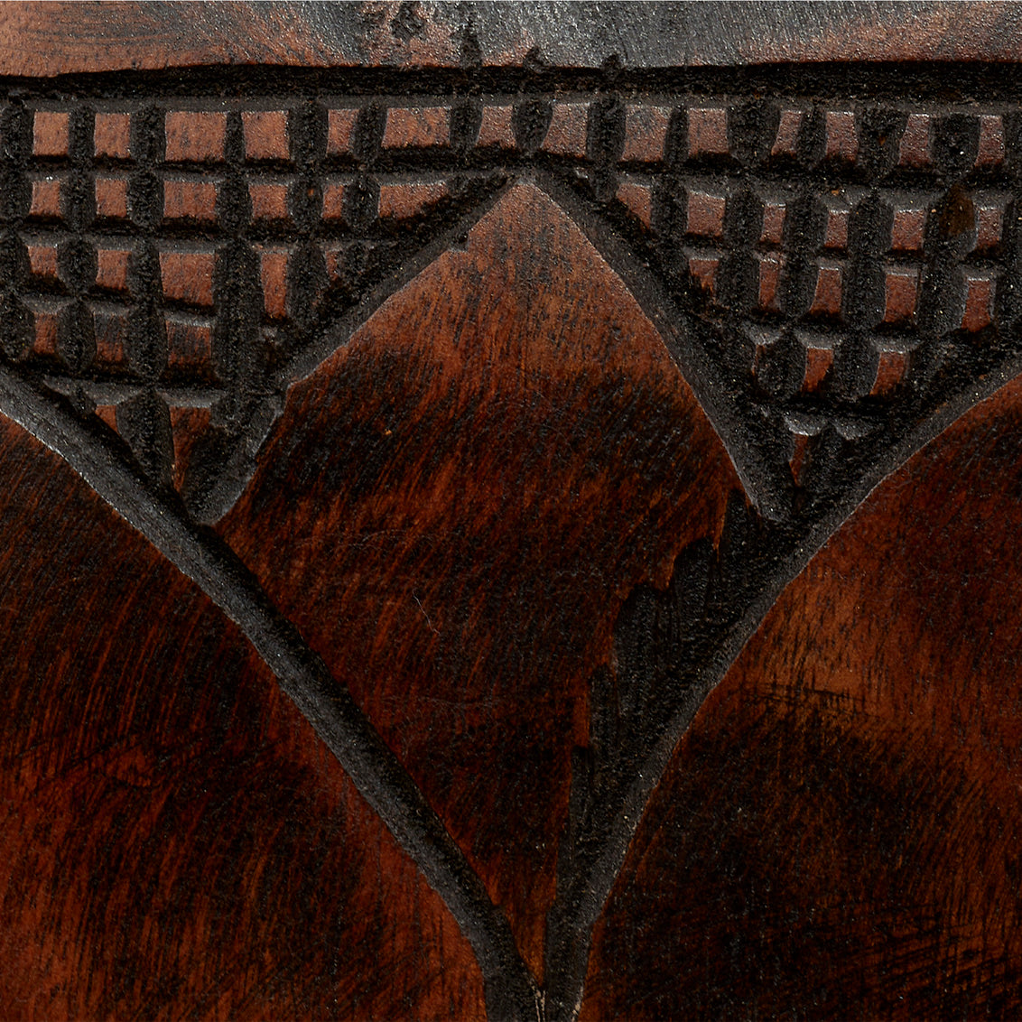 Close-up of a carved mango wood surface from the Totem Floor Lamp, featuring geometric patterns—including a triangular design and a grid-like motif above it. The dark, polished wood accentuates the intricate carvings characteristic of this artisan floor lamp.