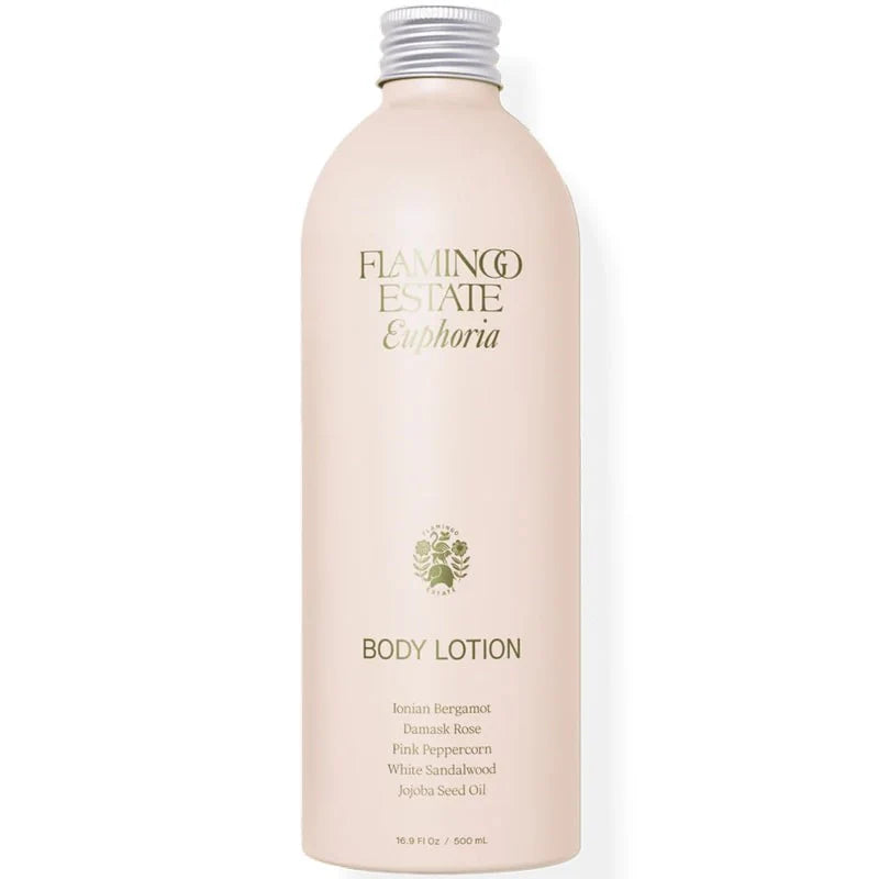 A tall, pale pink bottle labeled Flamingo Estate - Jasmine Damask Rose Body Lotion with gold text. Infused with essential oils, it contains Jasmine, Damask Rose, Pink Peppercorn, White Sandalwood, and Jojoba Seed Oil.