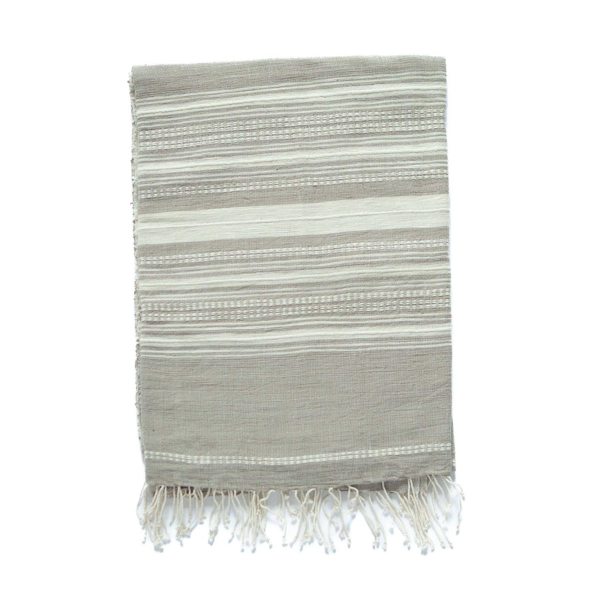 The Handwoven Ethiopian Cotton Hand Towel, featuring beige and white horizontal stripes and fringed edges, is eco-friendly and displayed flat on a white background.
