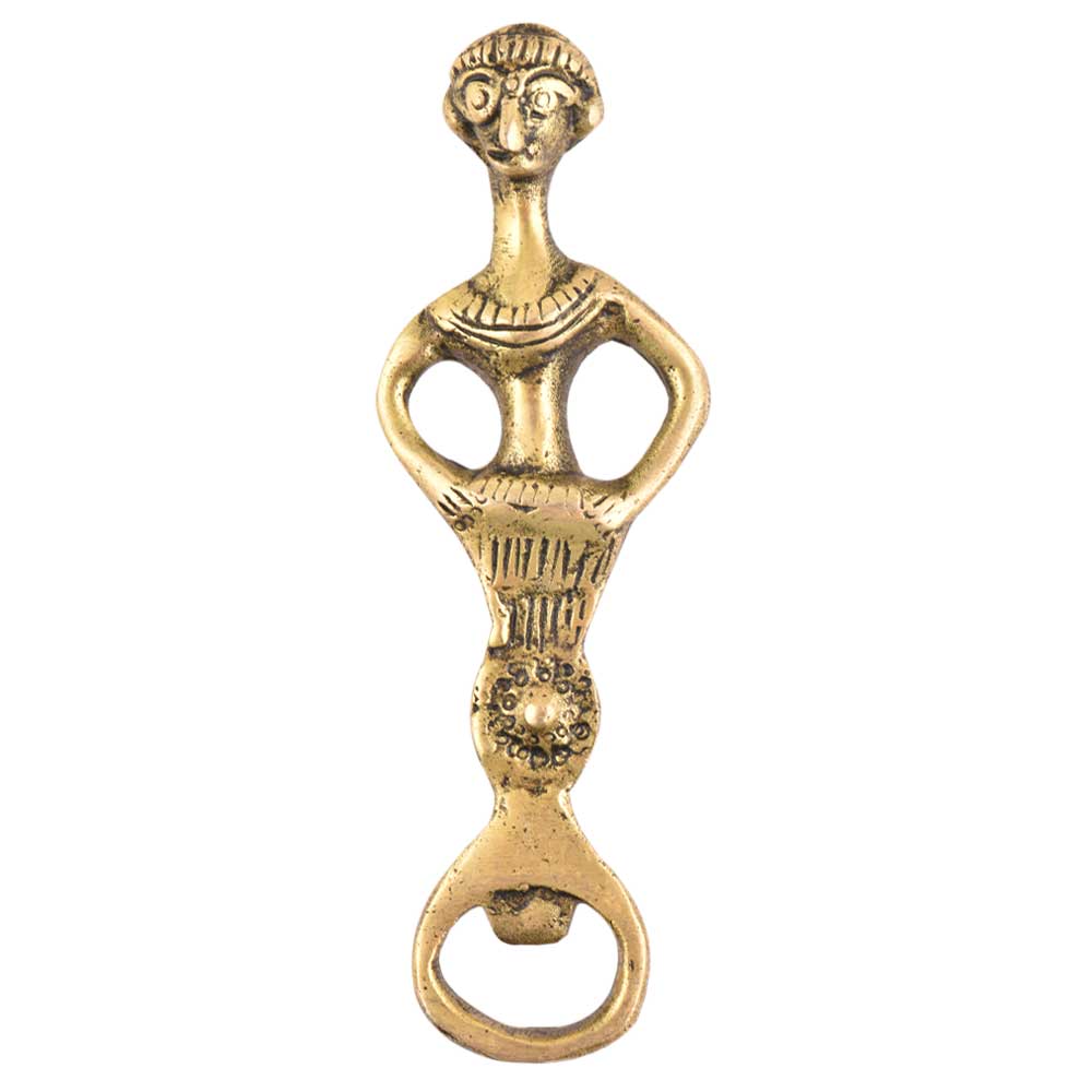 The Tribal Brass Bottle Opener features a stylized human figure with arms on hips, a textured skirt, and simple facial and hair details. Its dimensions are 13 cm x 3.8 cm x 0.4 cm.