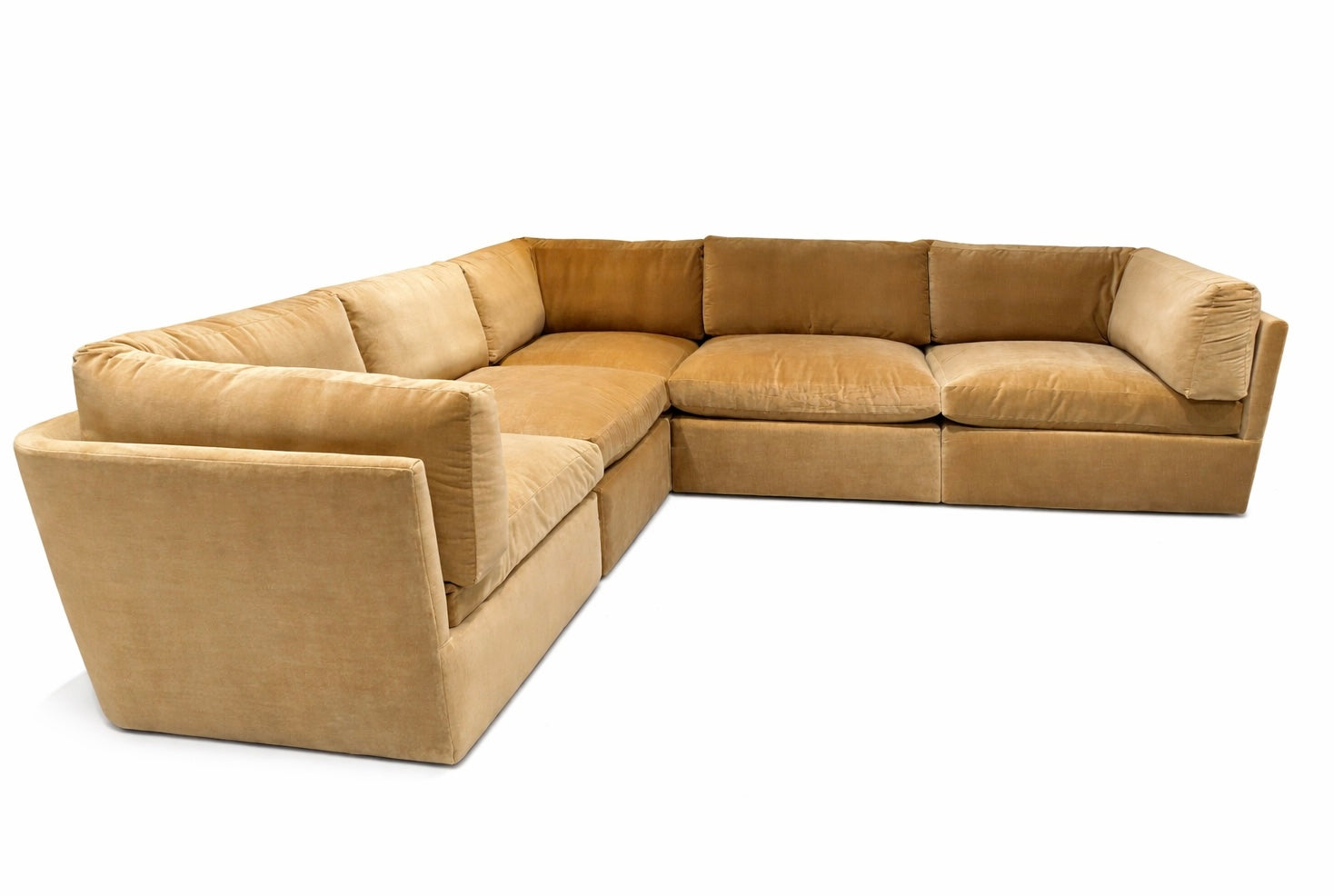 The Custom 5 pc Velvet Sectional is a spacious, L-shaped sofa with plush seats and backs, upholstered in soft light brown velvet. It’s available in multiple sizes and configurations for a cozy corner seating area.