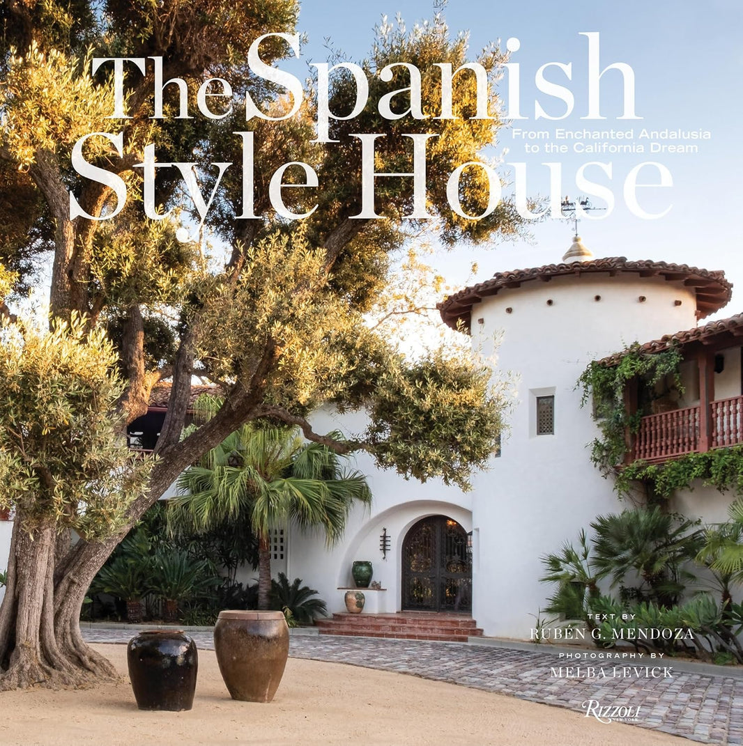 Front cover of The Spanish Style House, showcasing a classic Spanish-style home with white stucco walls, terracotta roof tiles, an arched door, a large tree, potted plants, and abundant greenery. This beautifully photographed 9″x9″ book by Ruben G. Mendoza and Melba Levick highlights the timeless elegance and charm of Spanish-style architecture.