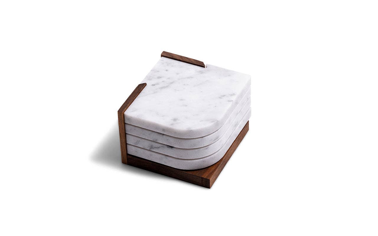 The Marble Coasters + Trivet set features four round-edged white marble coasters neatly stacked in a walnut stand, shown against a white background.