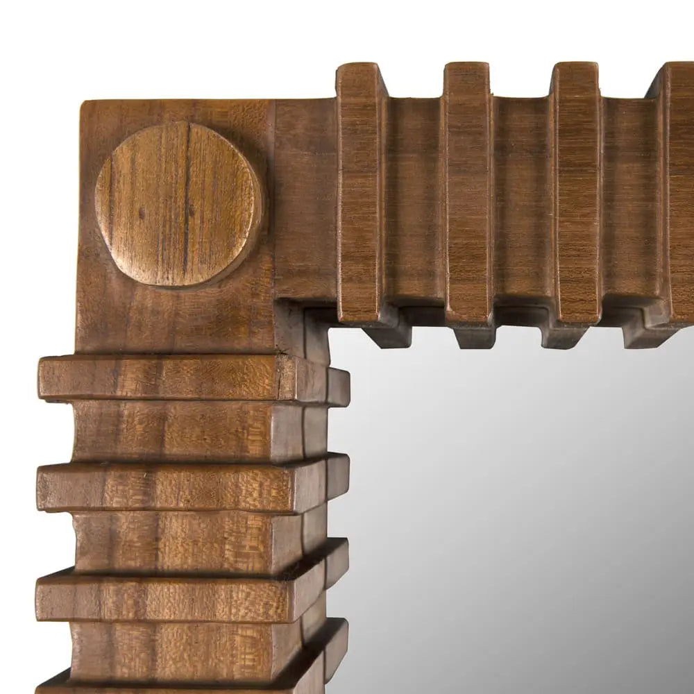 Close-up of the Sculpted Teak Mirror, featuring a geometric, layered wooden frame with a round accent in the corner. The warm natural teak finish reflects light on the right. Dimensions: 26W x 2D x 36H.