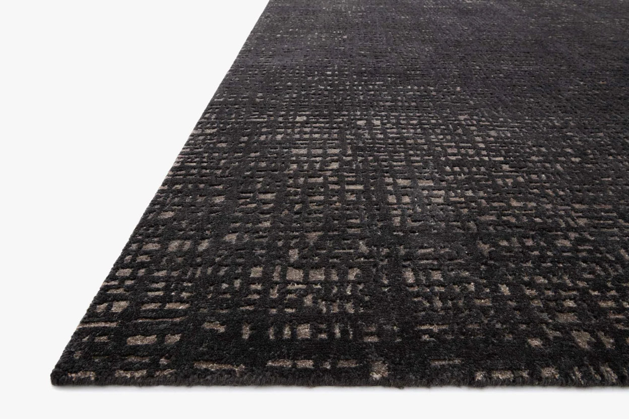 A close-up angled view of the Bark Rug (8'-6" x 11'-6"), a dark rectangular wool rug with a textured grid pattern in gray and black shades, set against a plain white background. Available in multiple sizes.