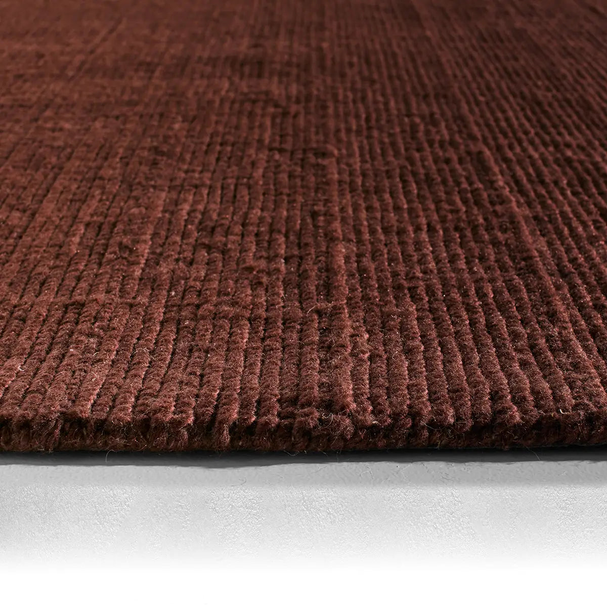 Close-up of the Maroon Handwoven Rug, featuring a ribbed texture and thick pile on a light-colored floor. The image highlights the plush fibers and depth, emphasizing the luxurious feel of this large area rug.