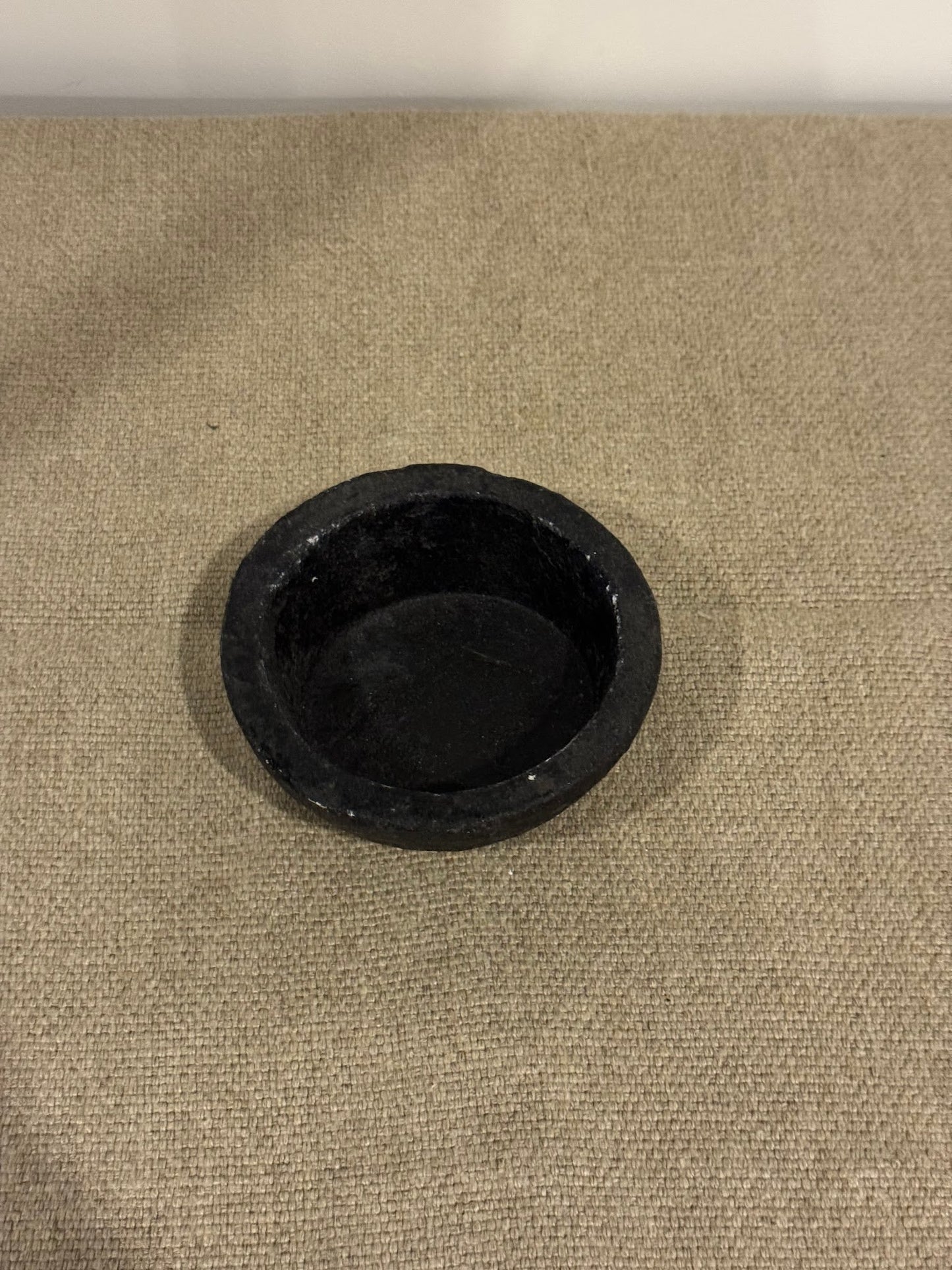A 5-inch wide Black Bowl with a round, shallow shape sits centered on a textured beige surface, set against a plain light-colored wall.