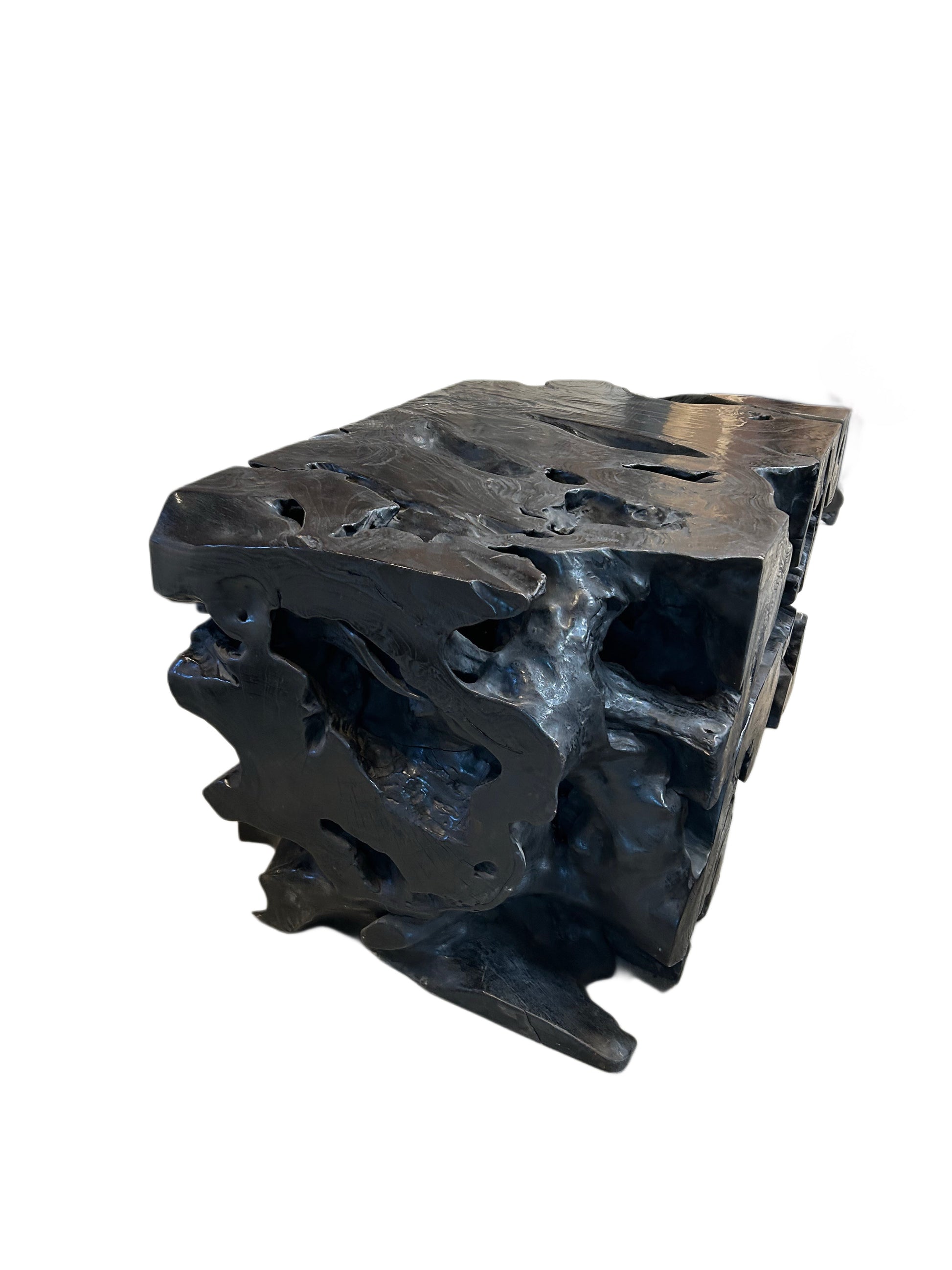 The EBONIZED OLD GROWTH TEAK STUMP is a sculpted black table made from an ebonized teak stump, featuring jagged edges, cave-like hollowed forms, and an irregular surface, set against a white background.